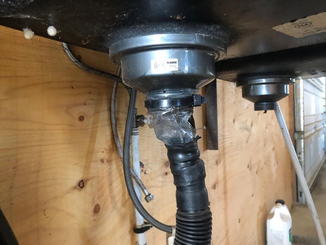 Underside of a black kitchen sink with plumbing. A black, flexible drain pipe is taped and connects to the drain.
