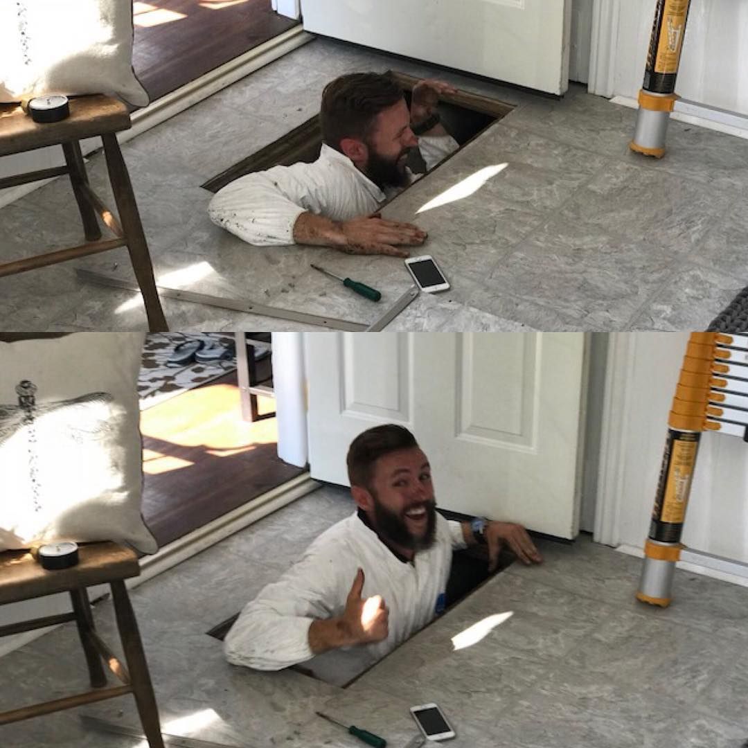 Man in white jumpsuit emerges from floor opening, smiling, giving thumbs up.