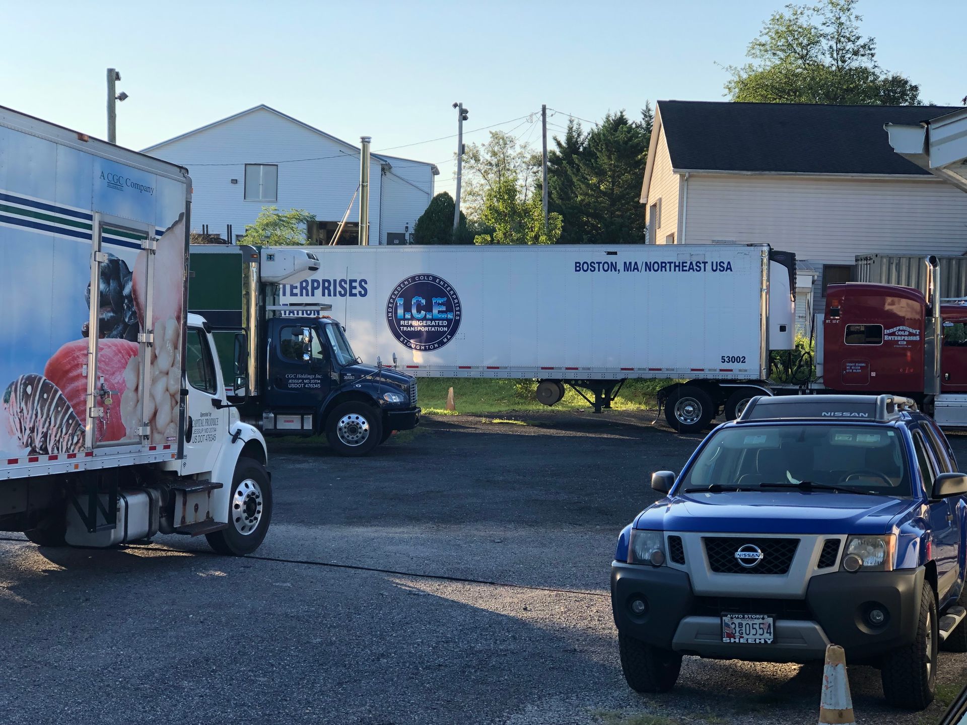 Trucks and a SUV parked in a lot. The trucks are white, the SUV is blue. A building is in the background.
