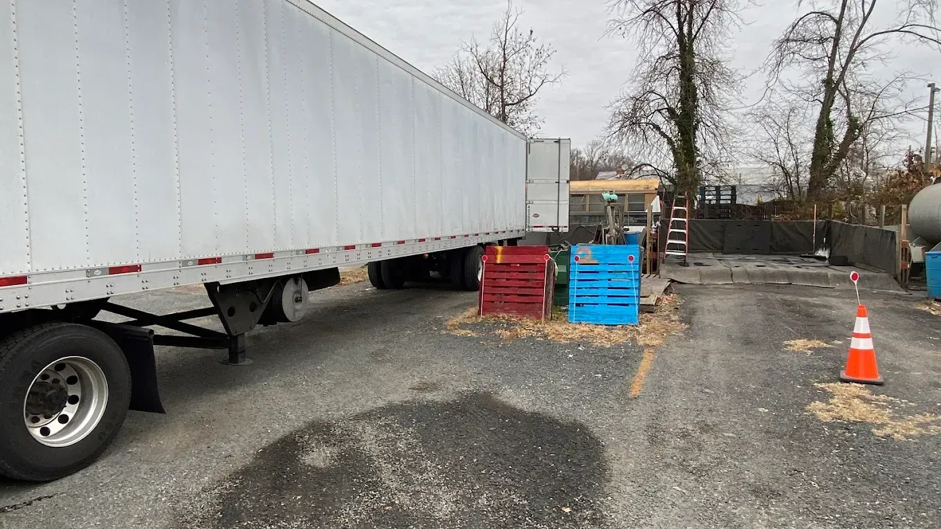 Semi-truck trailer parked on gravel, red and blue crates, and a traffic cone.