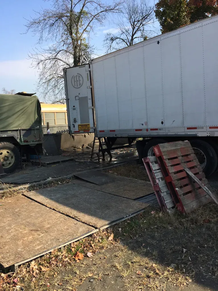 Truck trailer and military truck parked on mats, with pallets nearby.
