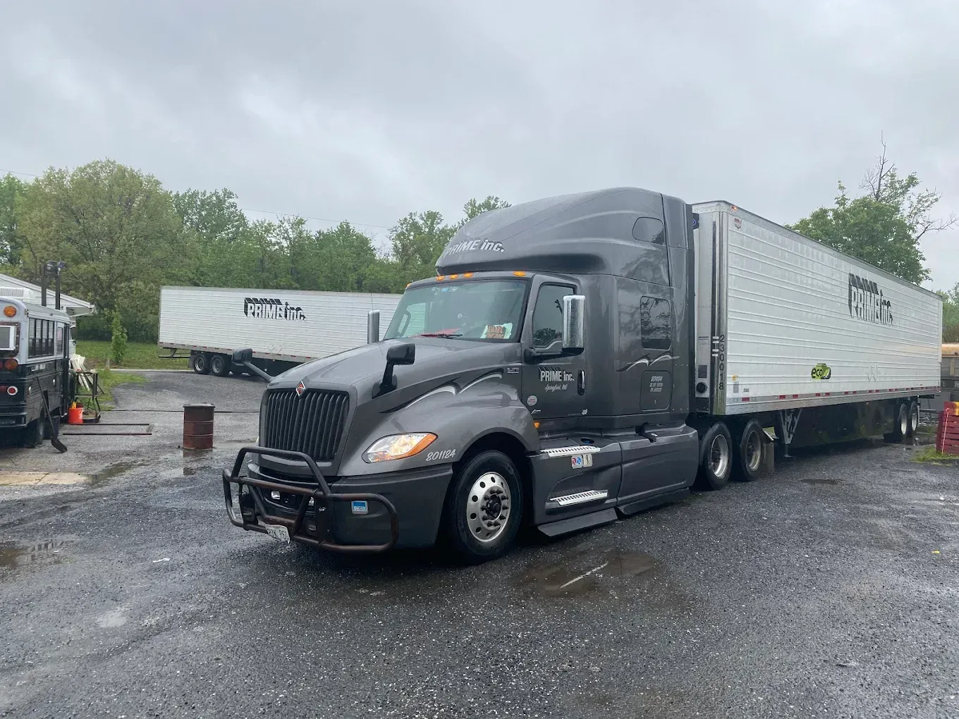 Dark gray semi-truck with a white trailer parked on wet pavement in front of a building.