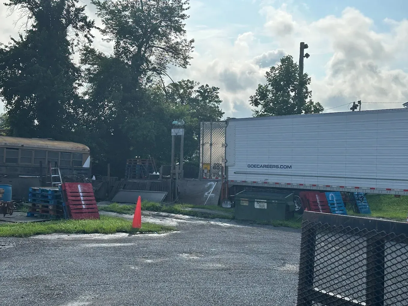 A parked semi-trailer and other industrial items on a gravel lot under a cloudy sky.