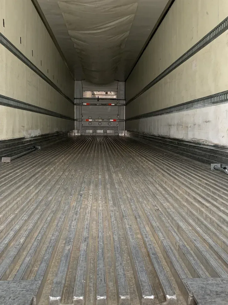 Empty semi-trailer interior with ribbed floor and white walls, viewed from inside towards the back.