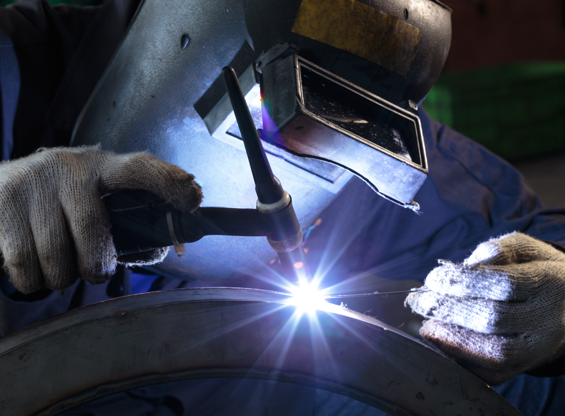 A man wearing a welding mask is welding a piece of metal
