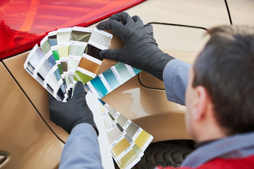 A man in black gloves is looking at a palette of paint colors on a car.
