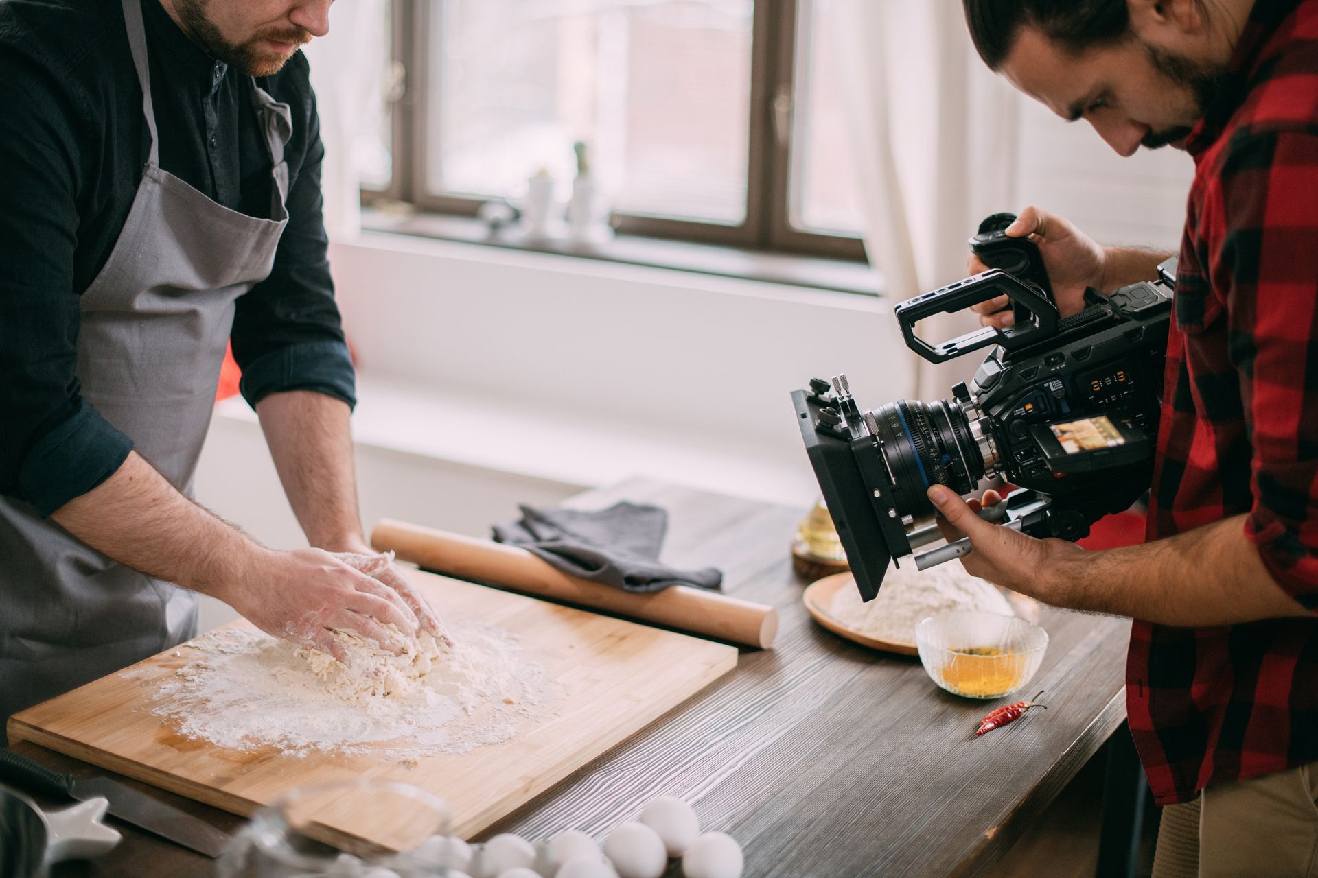 a man is rolling dough on a cutting board while another man takes a video with a camera