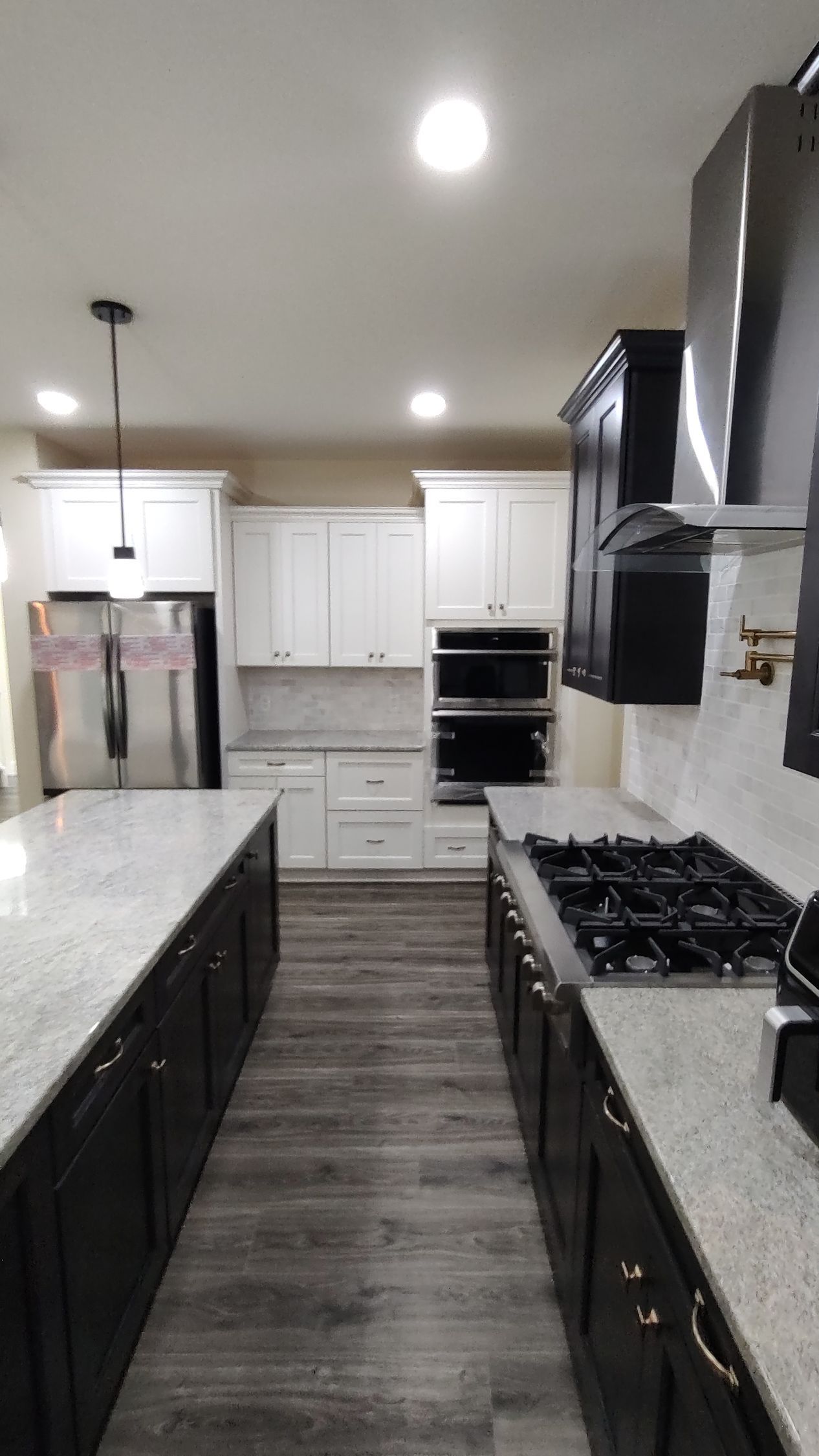 A kitchen with black cabinets , white cabinets , a stove top oven , a refrigerator , and a sink.