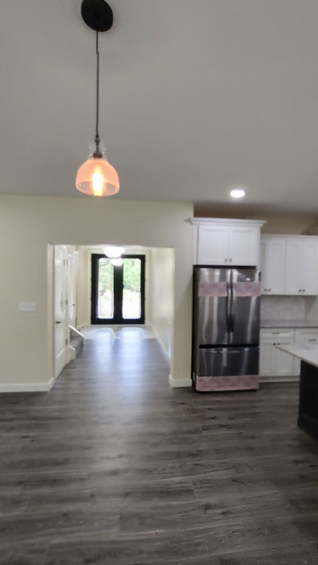 An empty kitchen with a stainless steel refrigerator and a light hanging from the ceiling.