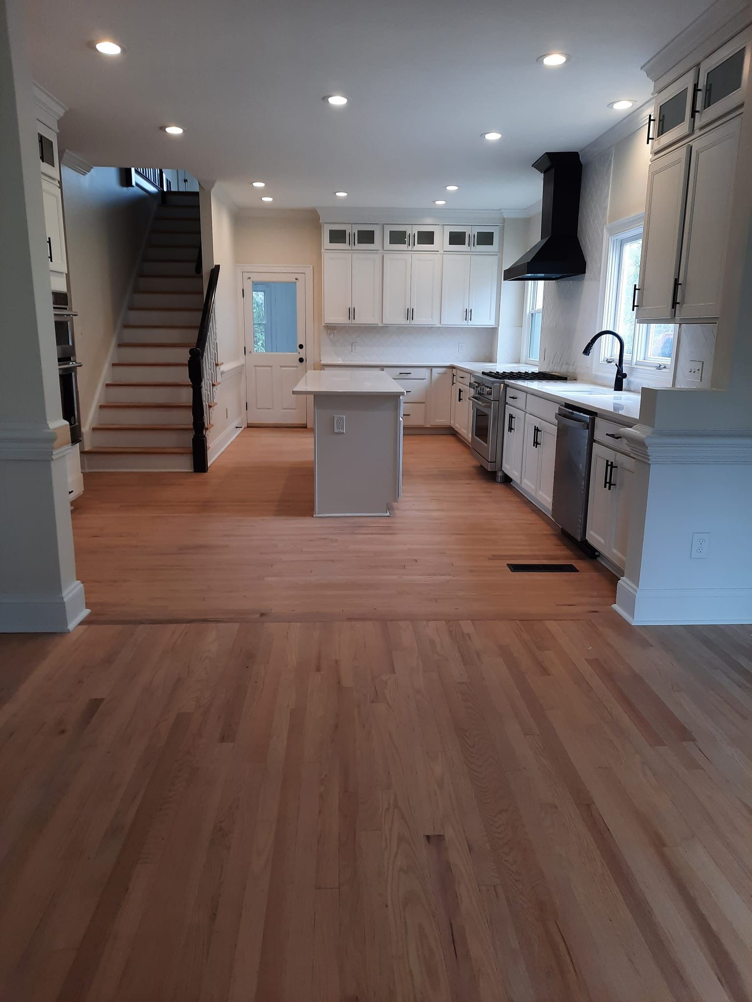 A kitchen with hardwood floors , white cabinets and stainless steel appliances.