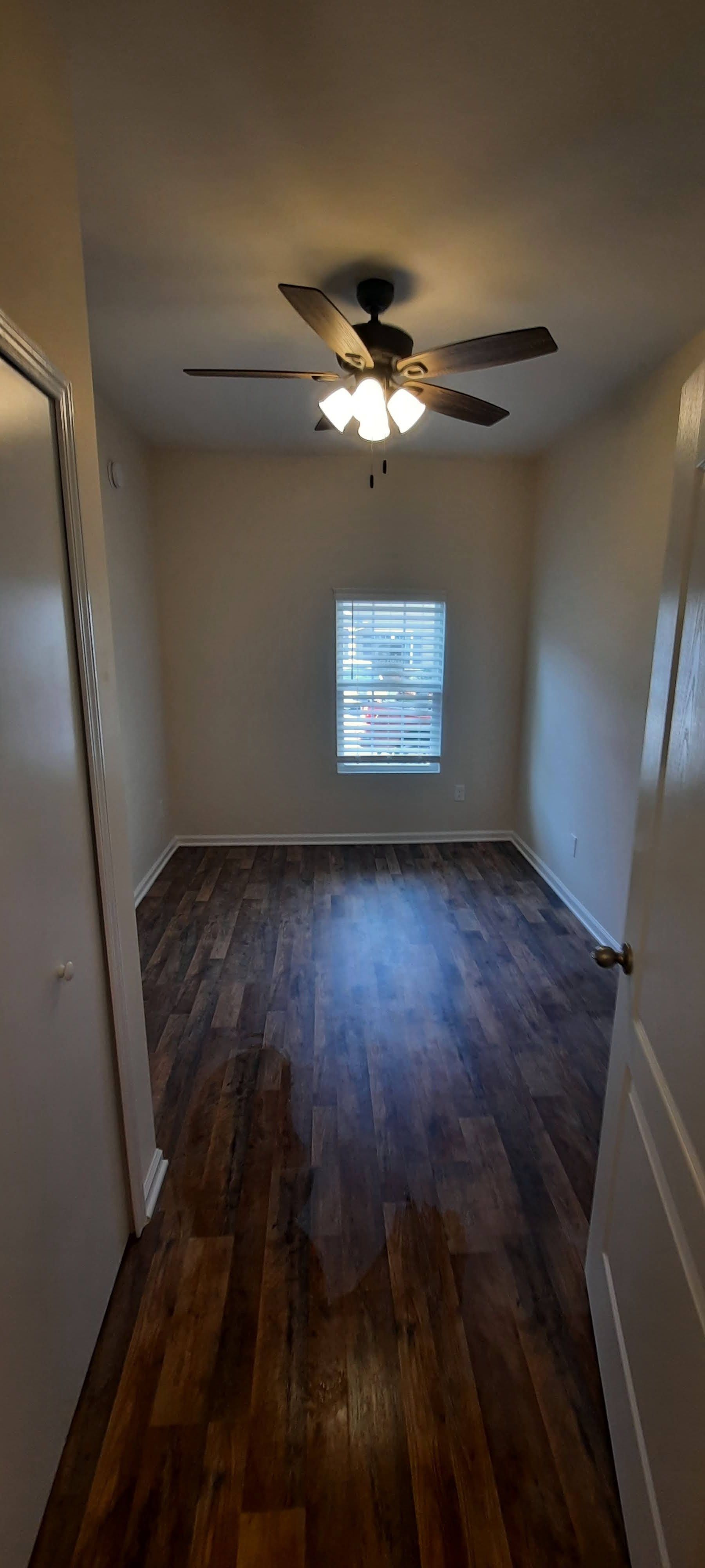 An empty room with a ceiling fan and a window.