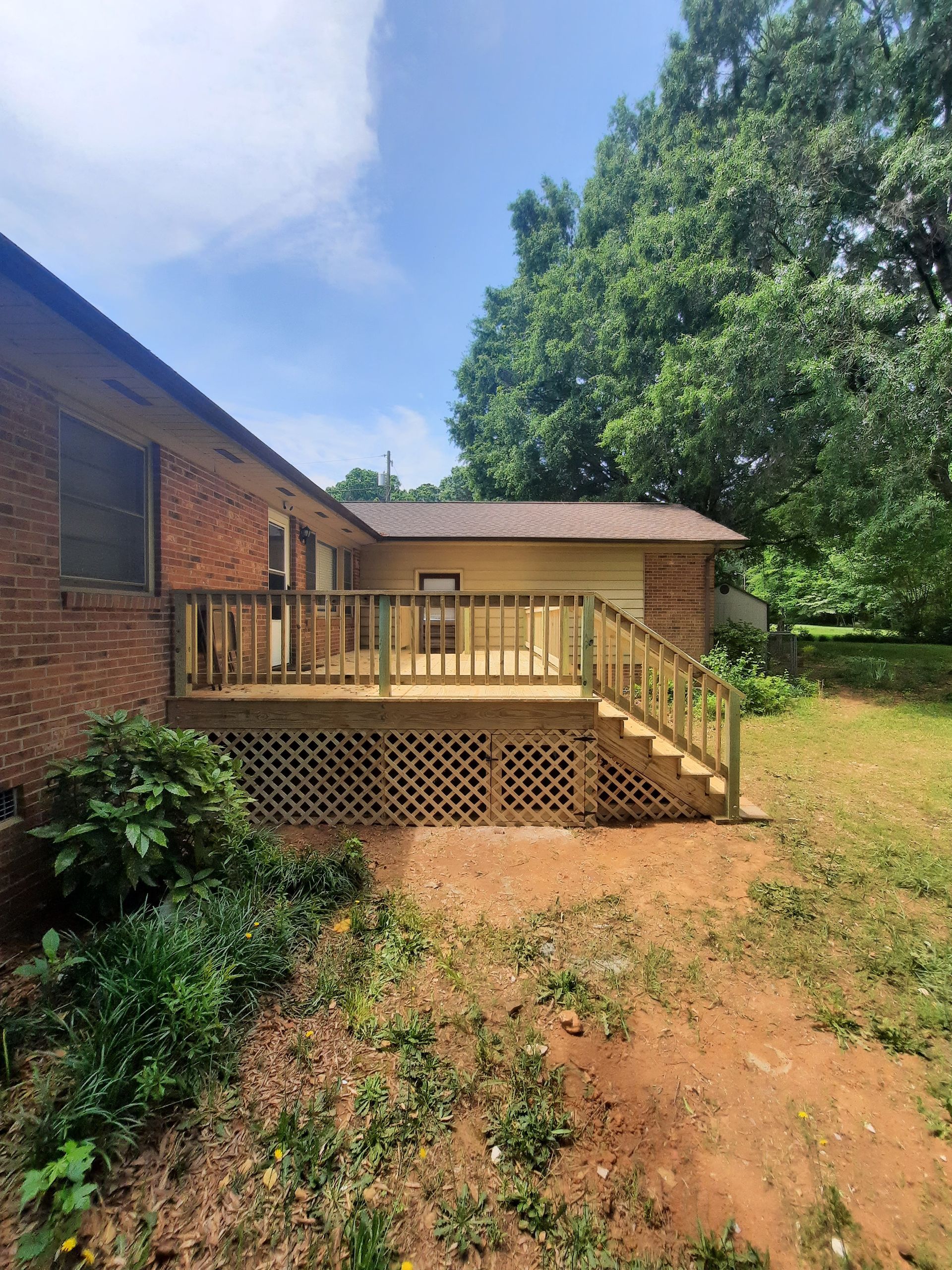 A brick house with a wooden deck and stairs in the backyard.