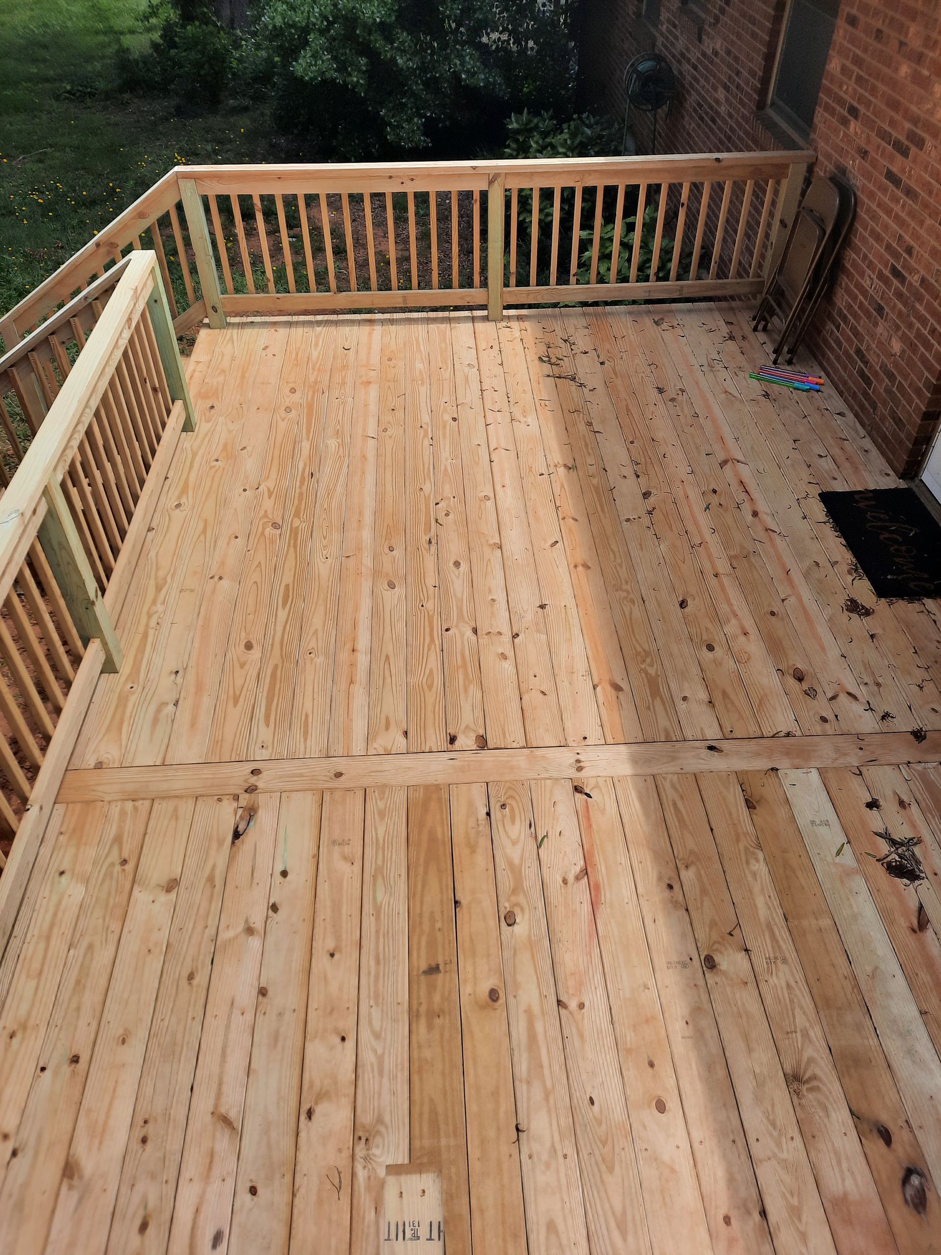 A wooden deck with a railing and a brick building in the background.