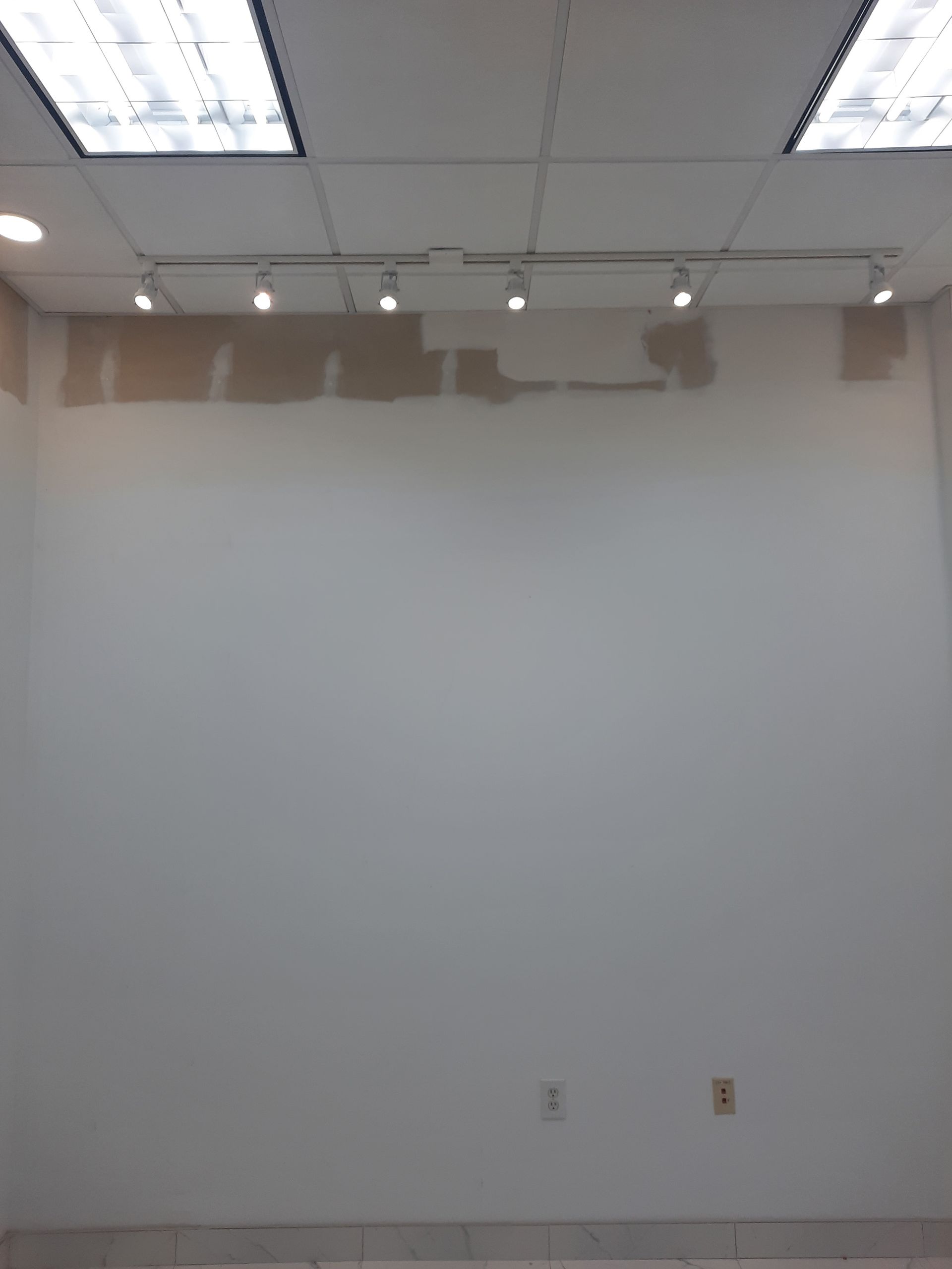 An empty room with a white wall and lights on the ceiling