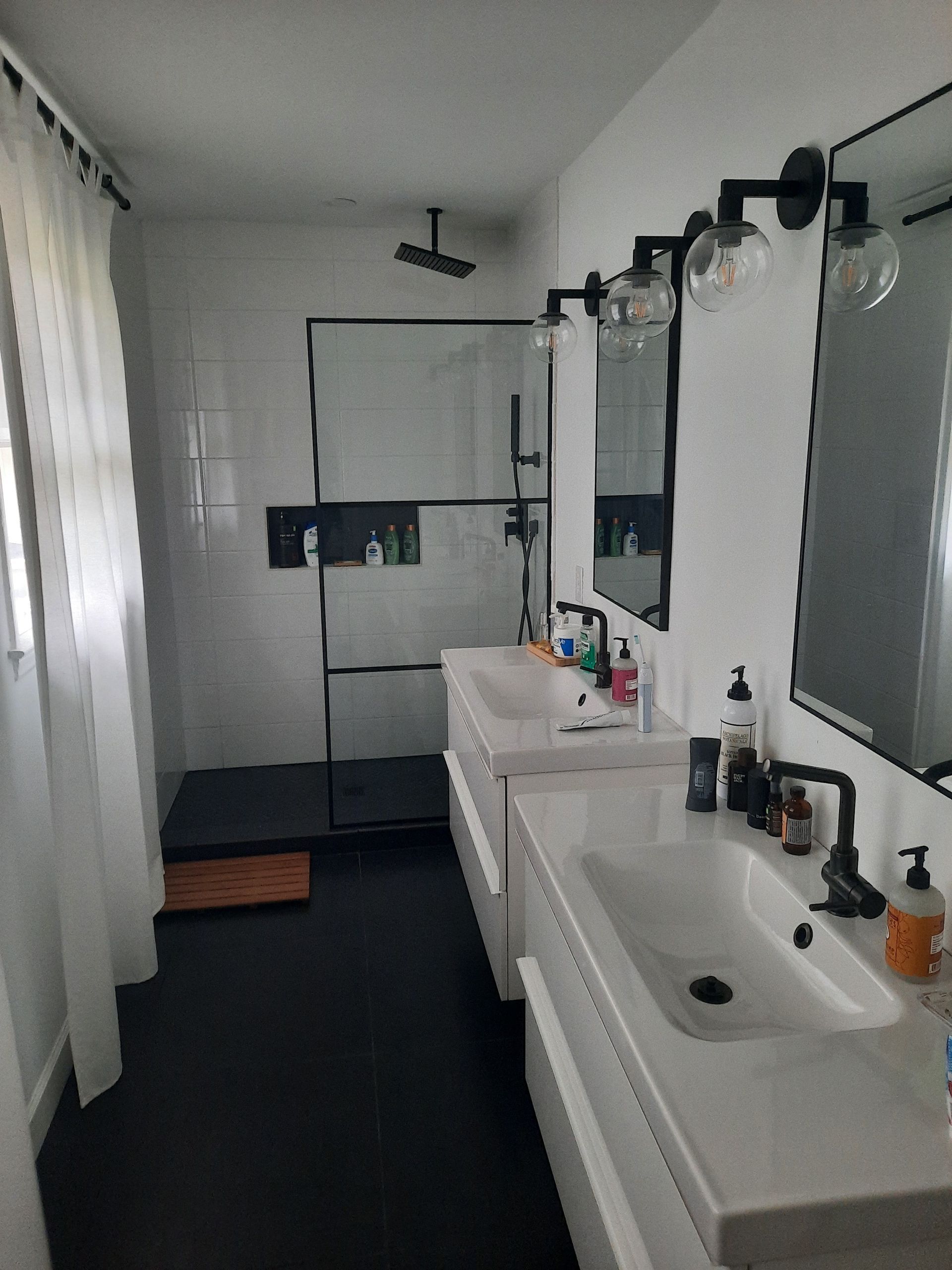 A bathroom with two sinks , two mirrors and a shower.