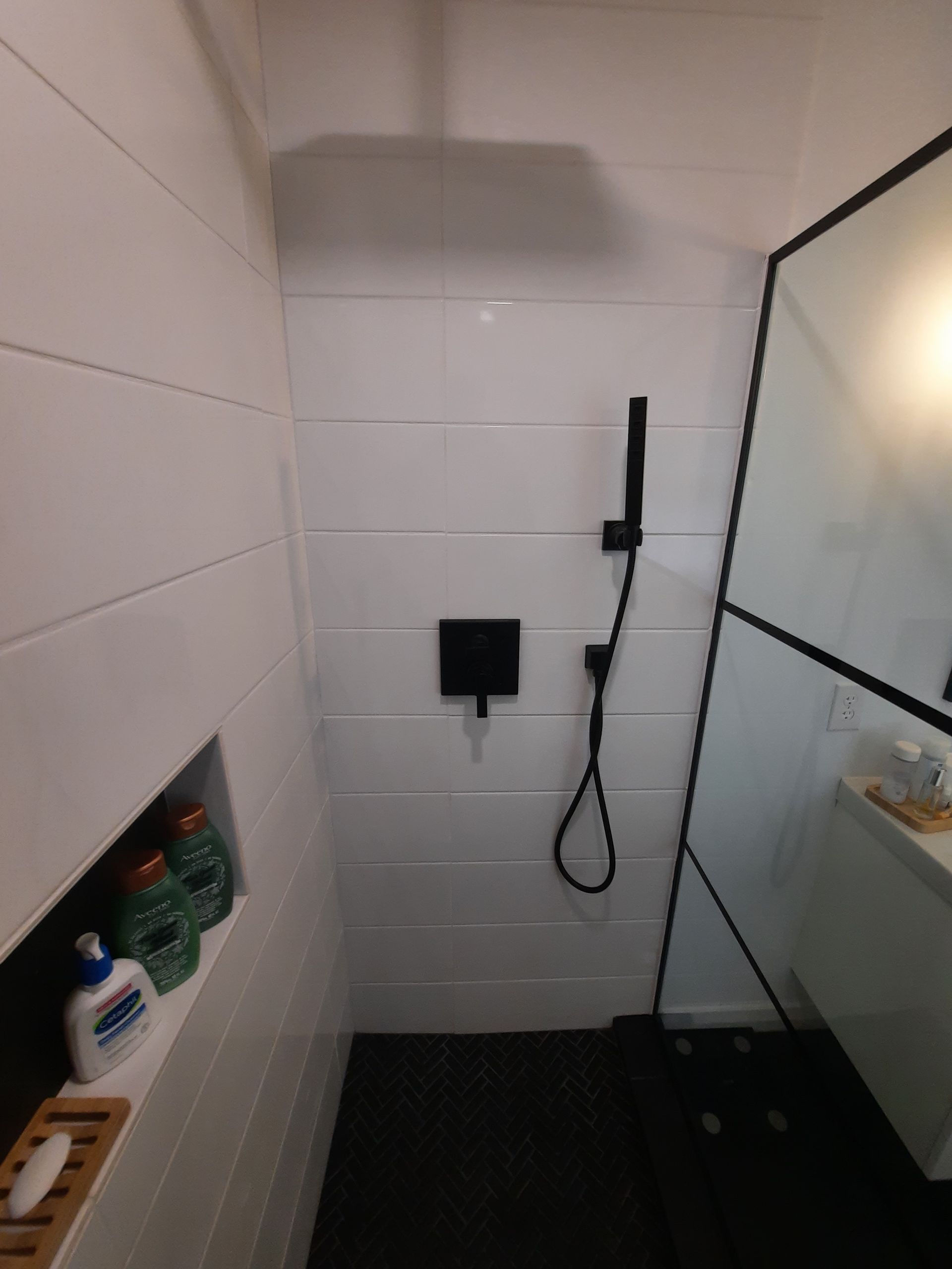 A bathroom with white tiles and a black shower head