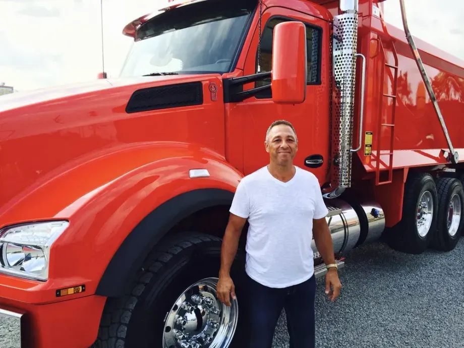 Man standing next to a large red dump truck. 