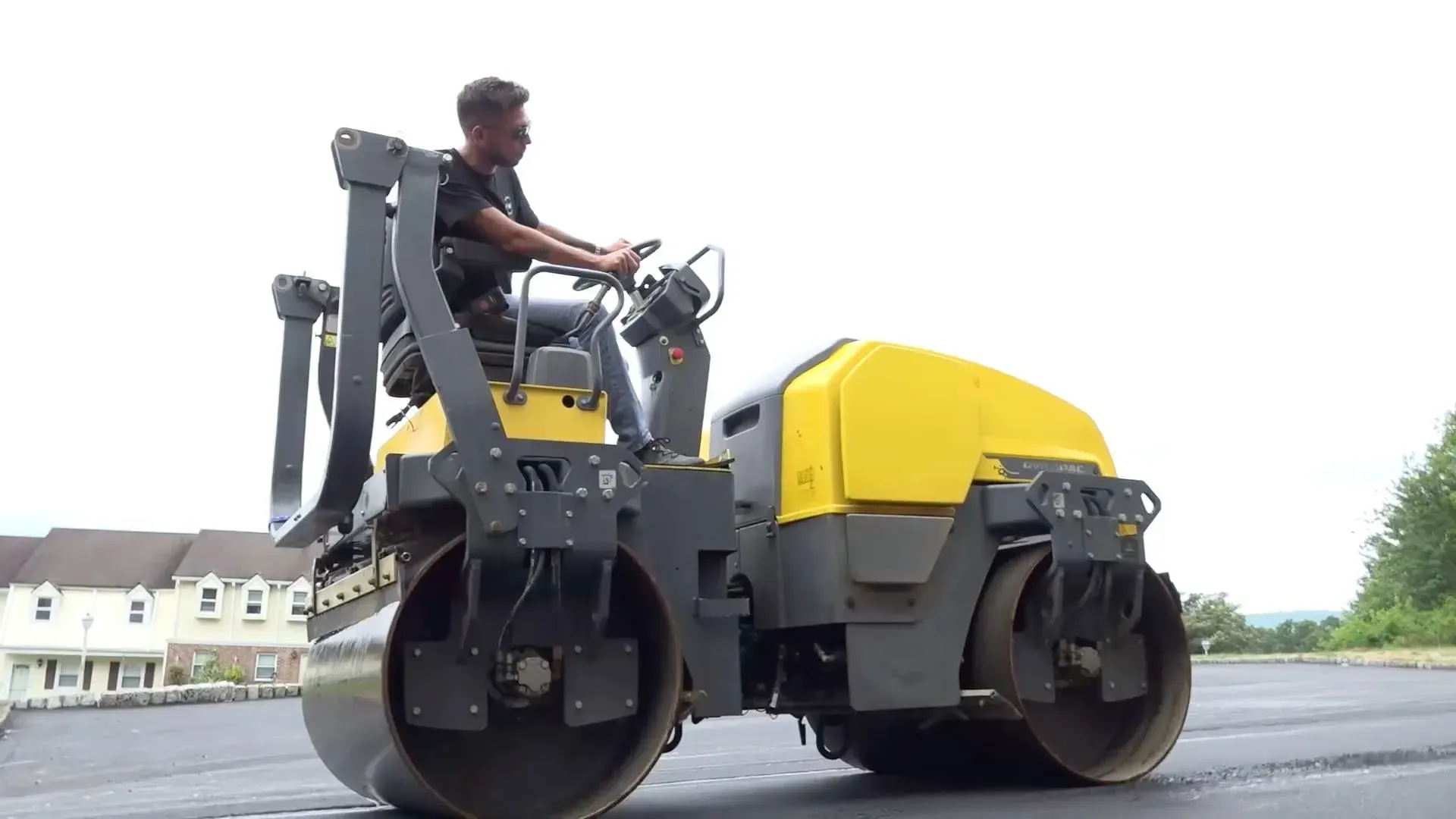 A person operating a yellow and black road roller, compacting fresh asphalt.