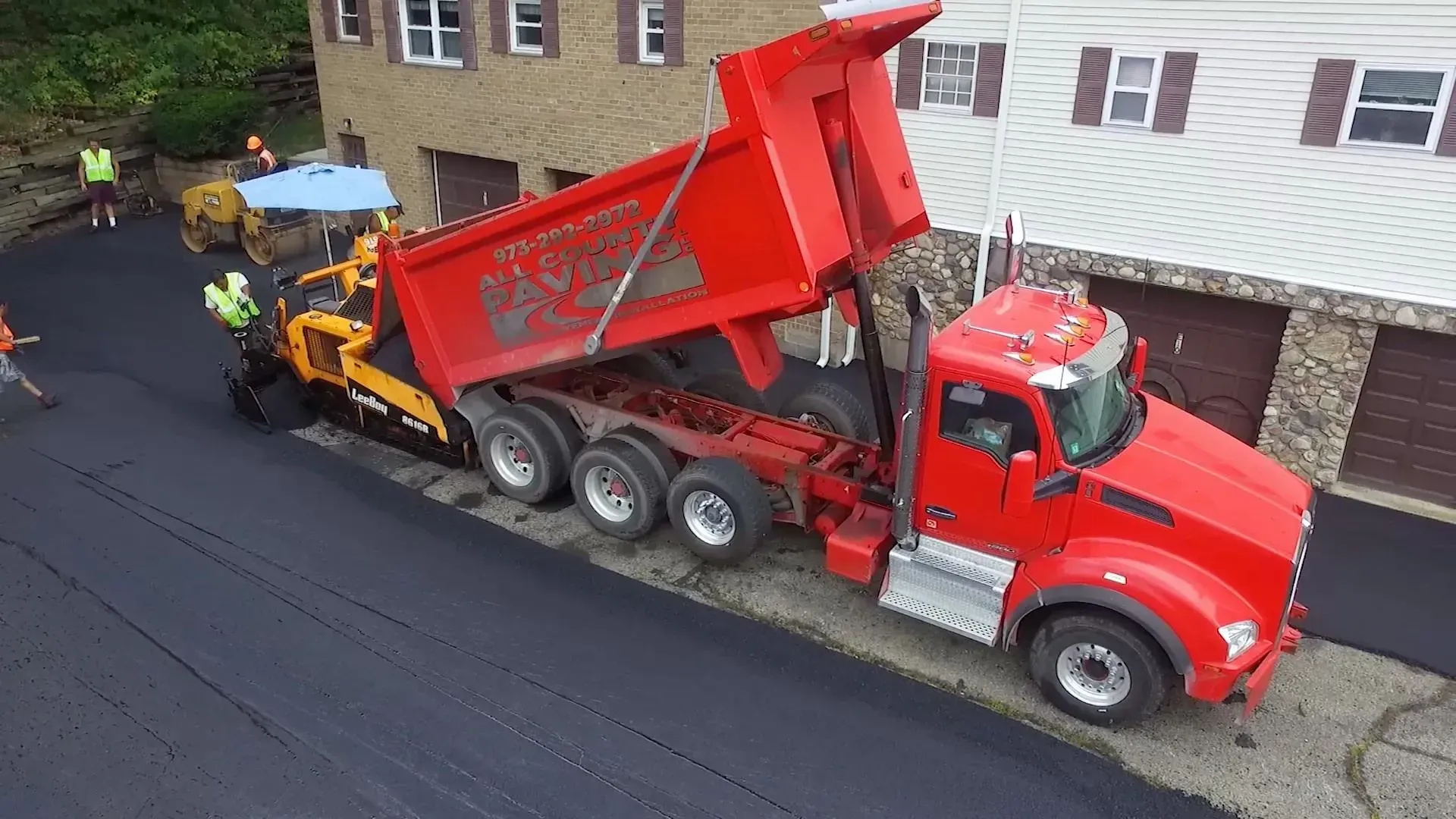Red dump truck unloading asphalt onto a road being paved.