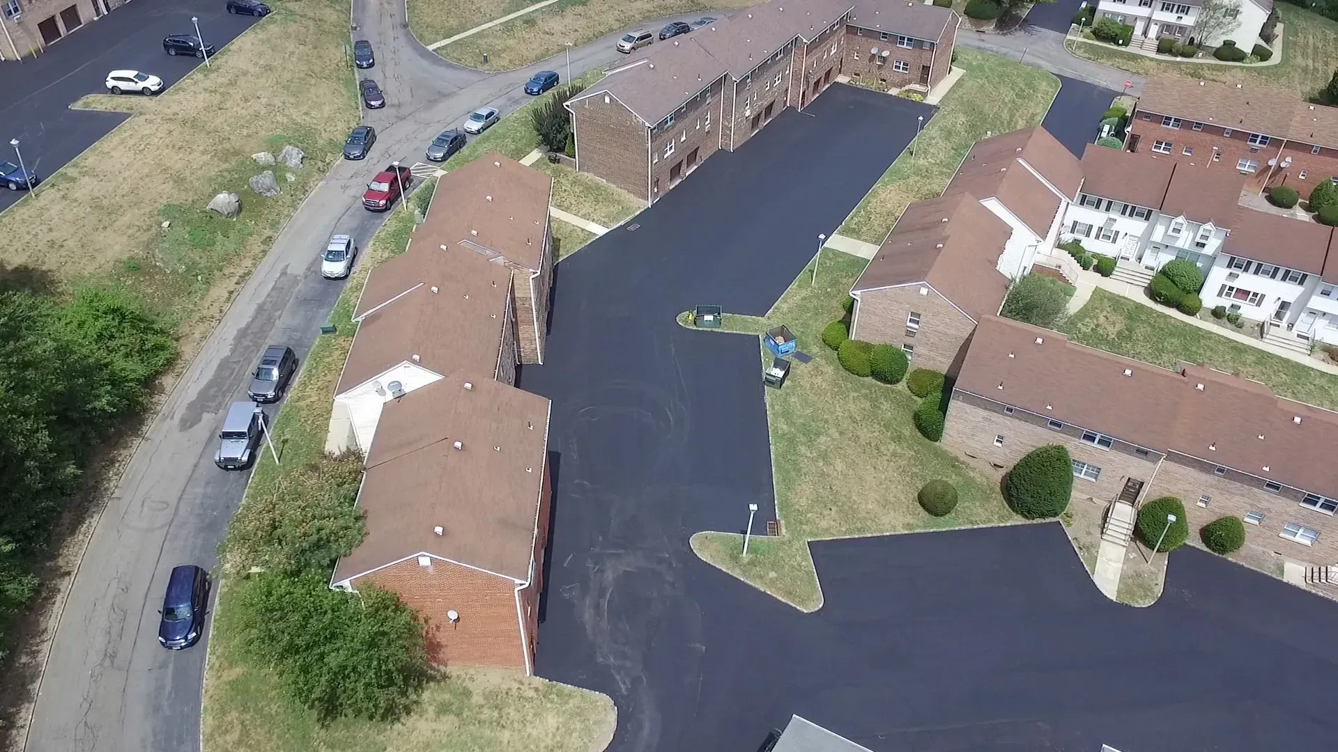 Aerial view of brick apartment buildings with brown roofs and black asphalt parking lots. 