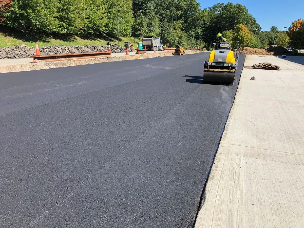A road paving project with a road roller compacting fresh black asphalt.