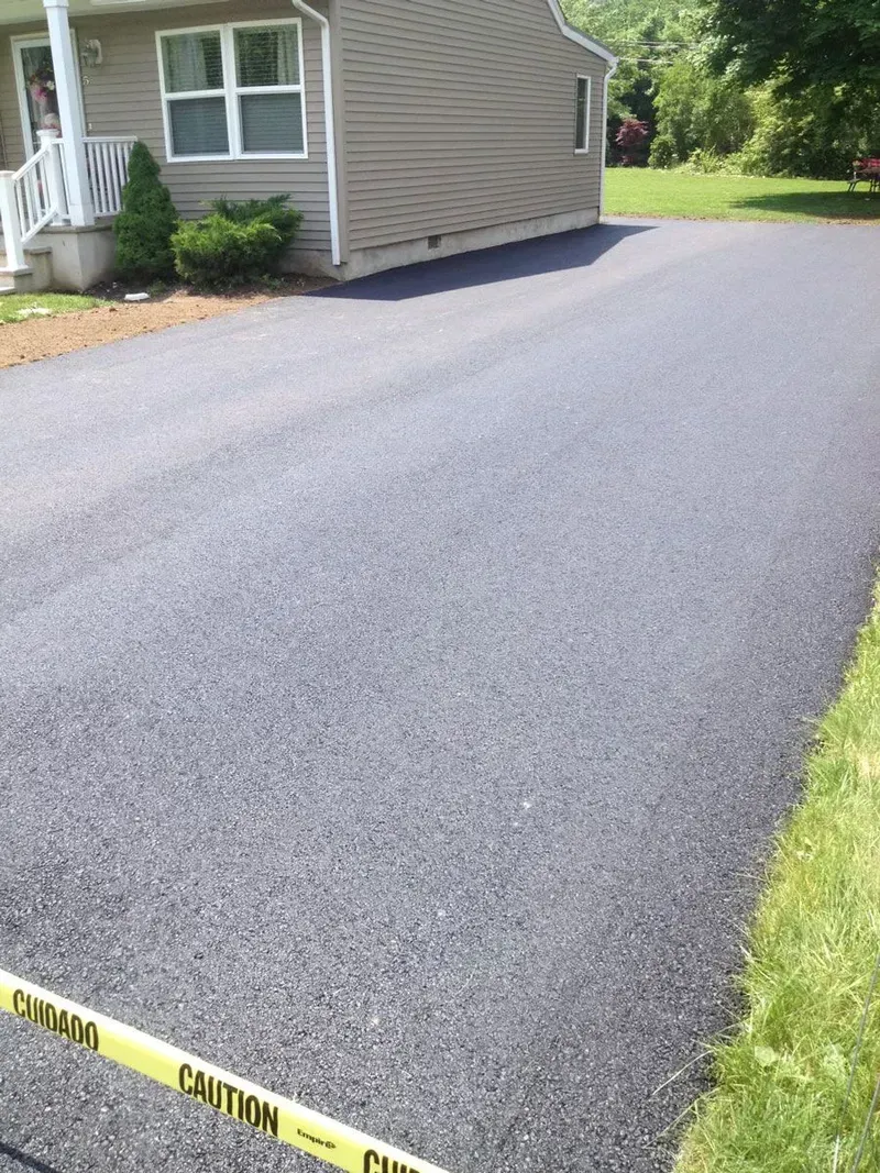 Freshly paved asphalt driveway in front of a beige house with white trim. 