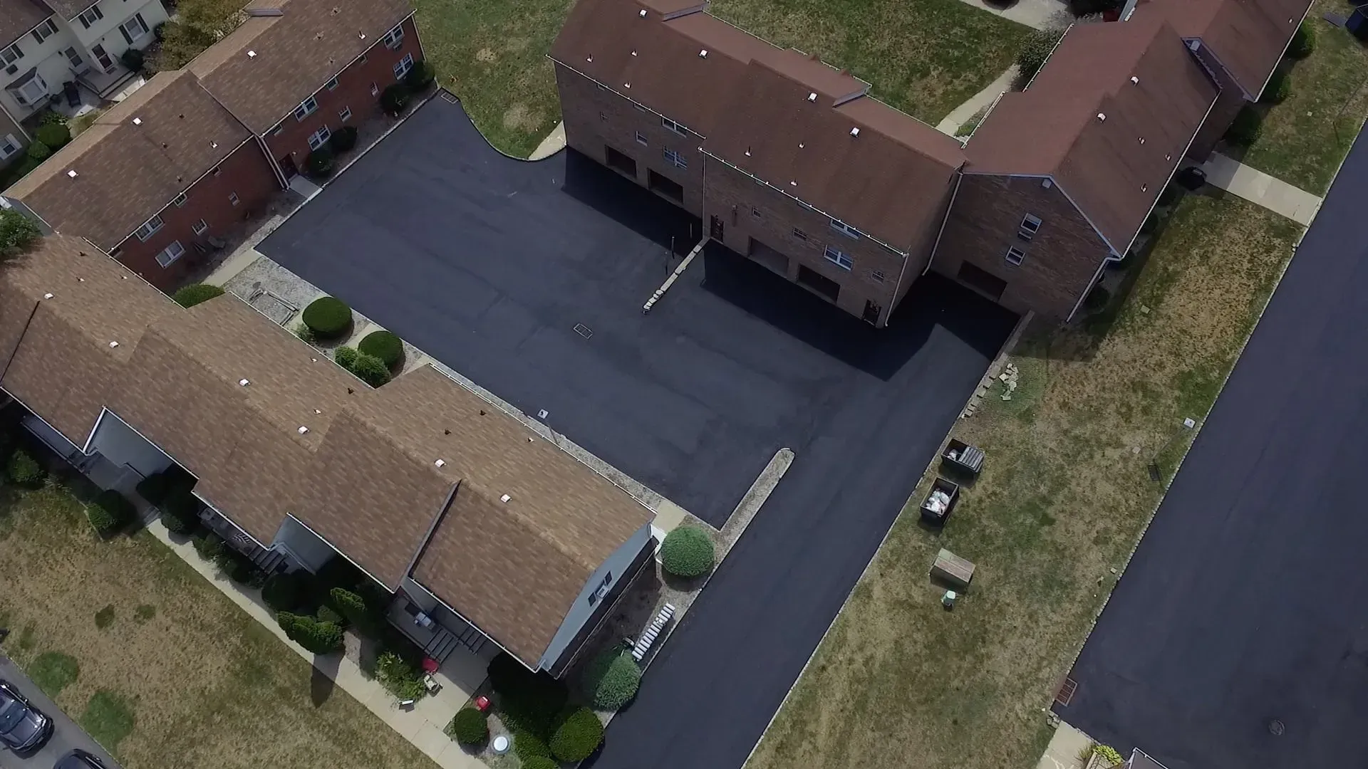 Aerial view of a brick apartment complex with brown roofs, asphalt parking, and green grassy areas.