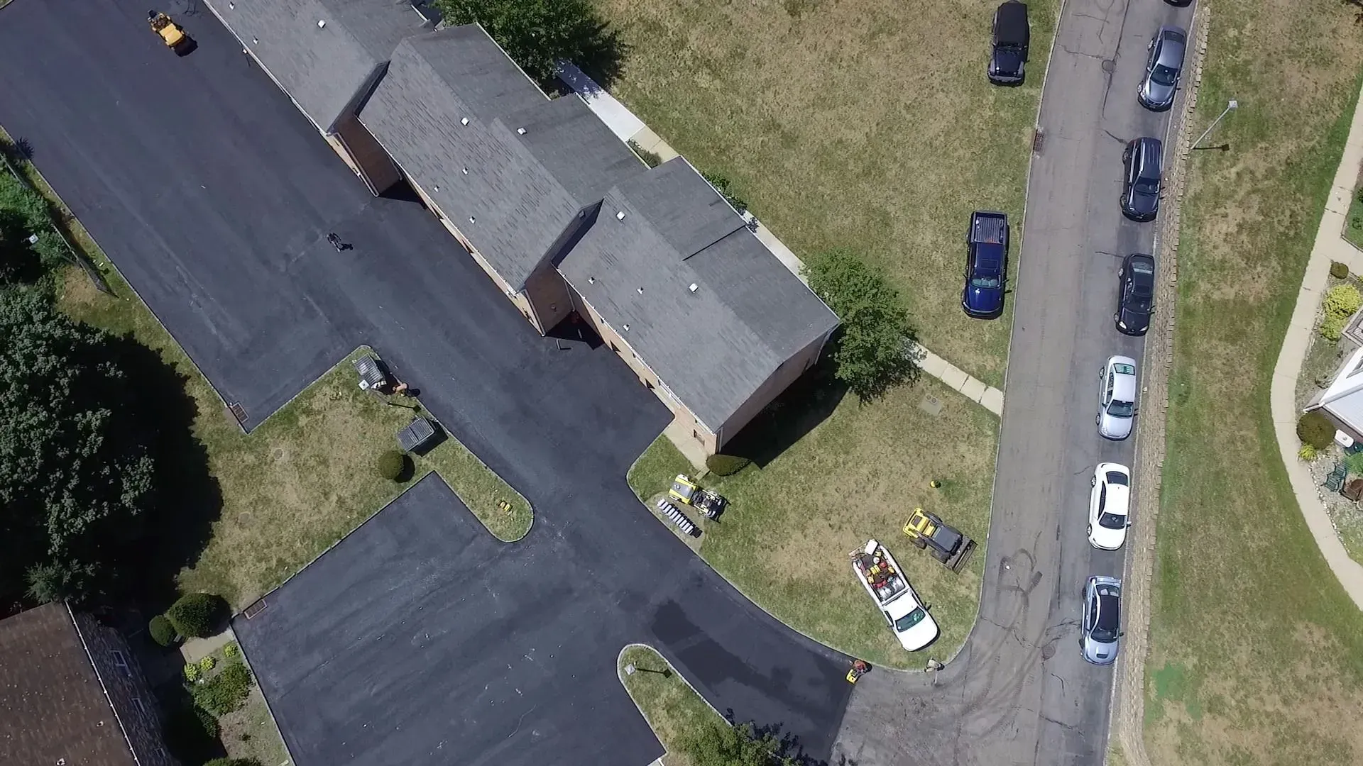 Aerial view of townhouses and parked cars along a street on a sunny day. 