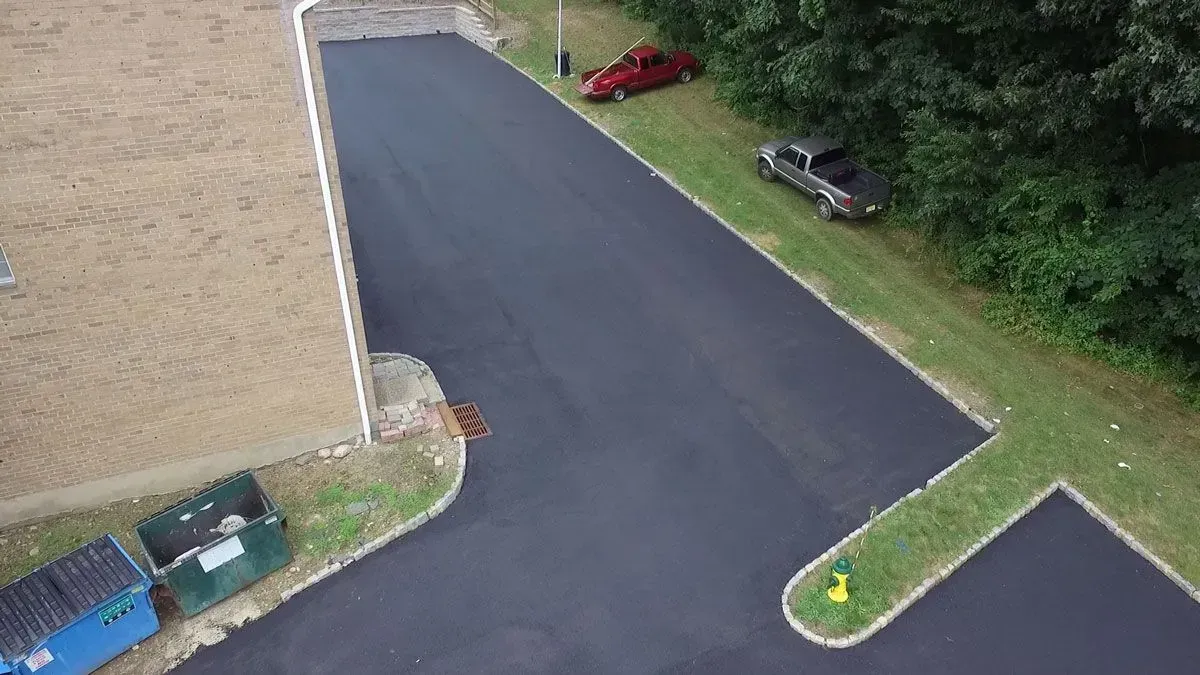 Aerial view of a newly paved asphalt driveway with parked trucks along the green grassy edges.