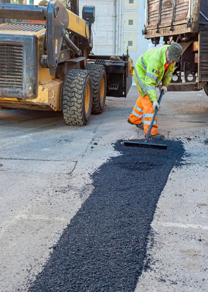 A road worker rakes fresh asphalt on a street. 