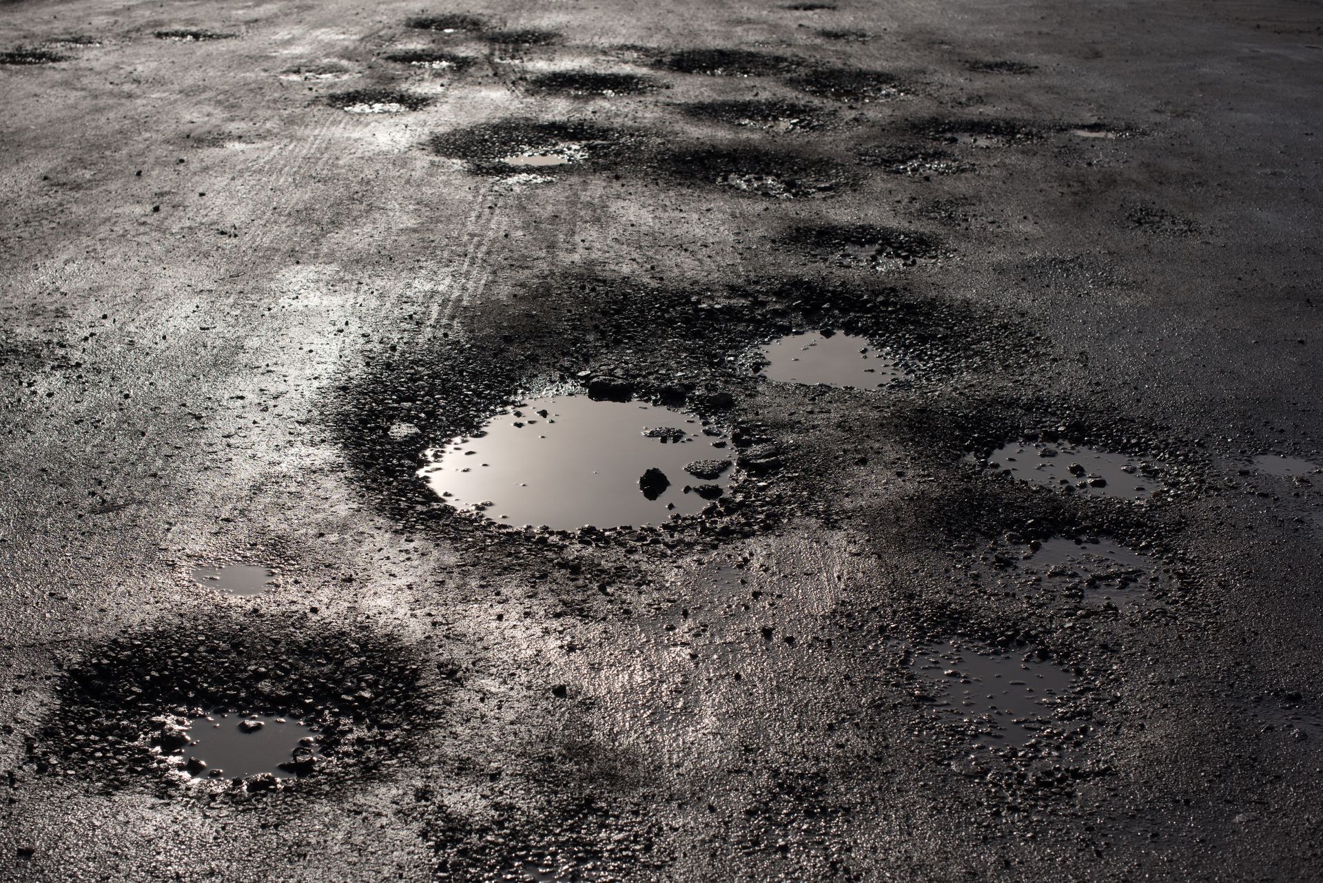 Dark asphalt road surface with many water-filled potholes.