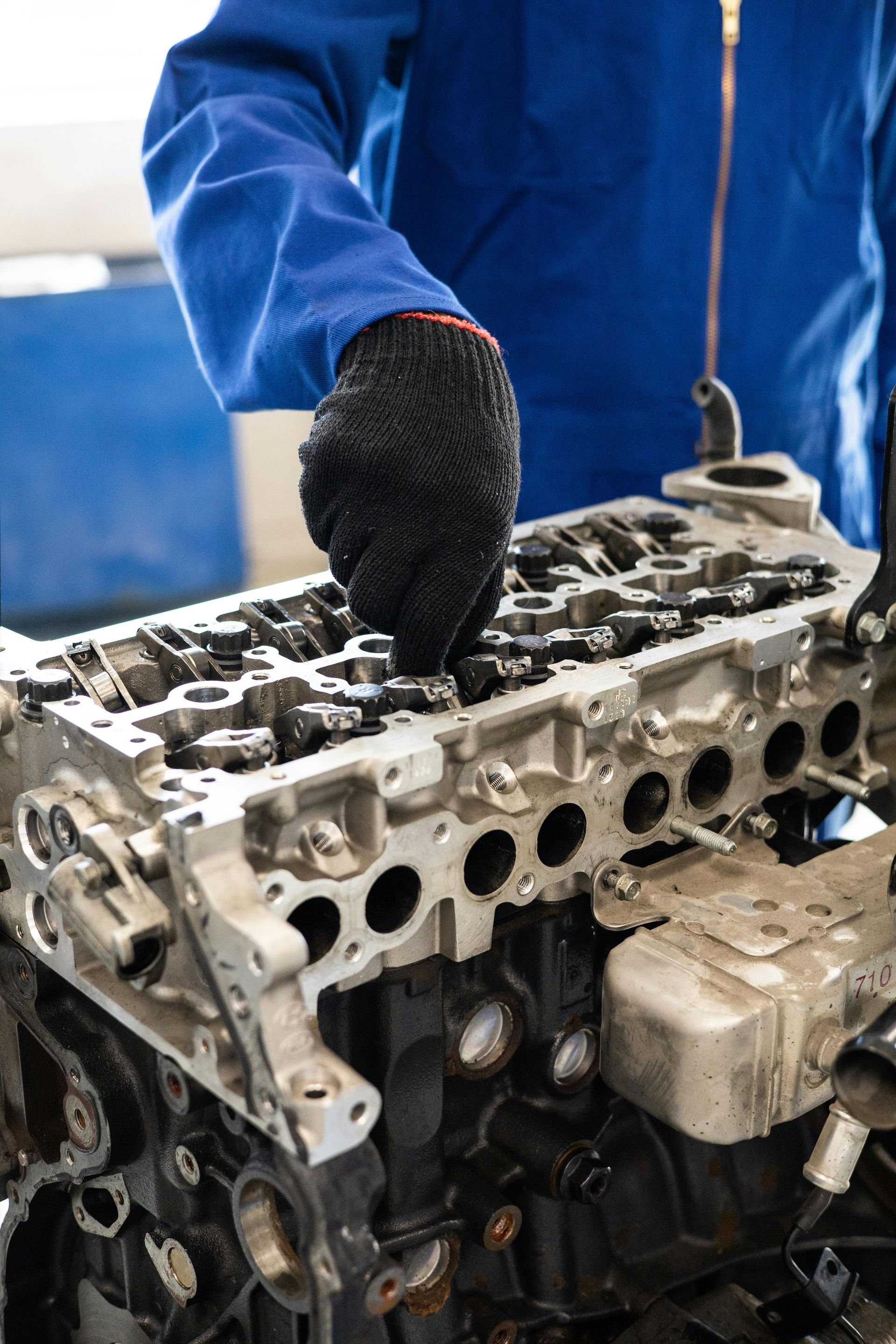 Mechanic in blue coveralls and black gloves works on an engine block.