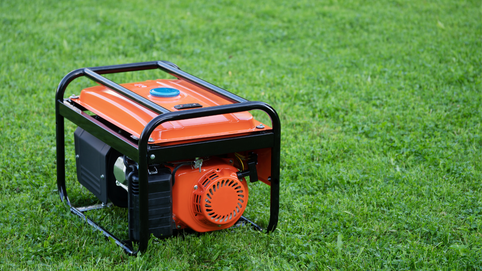 An orange portable generator is sitting on top of a lush green field.