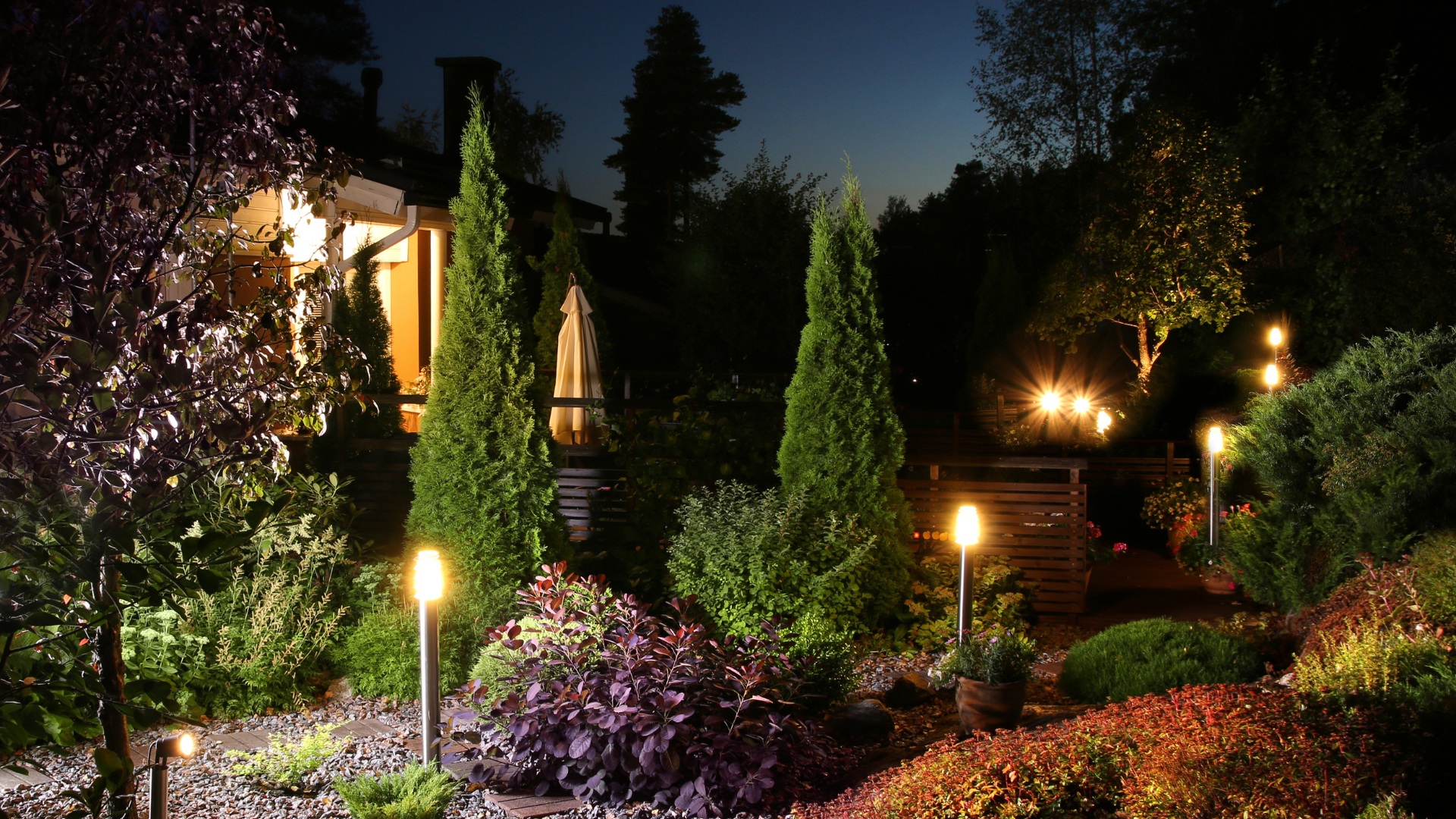 A garden is lit up at night with a house in the background