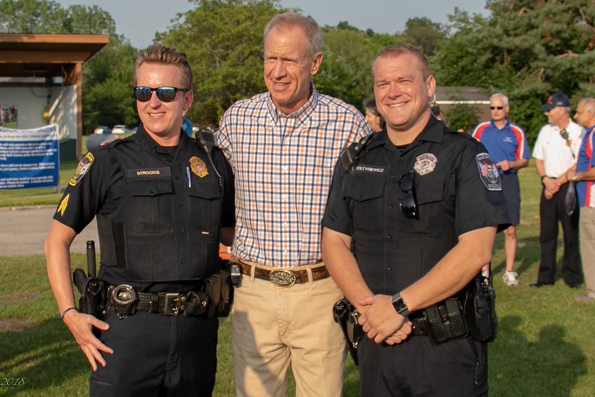 Three police officers are posing for a picture with a man in a plaid shirt.