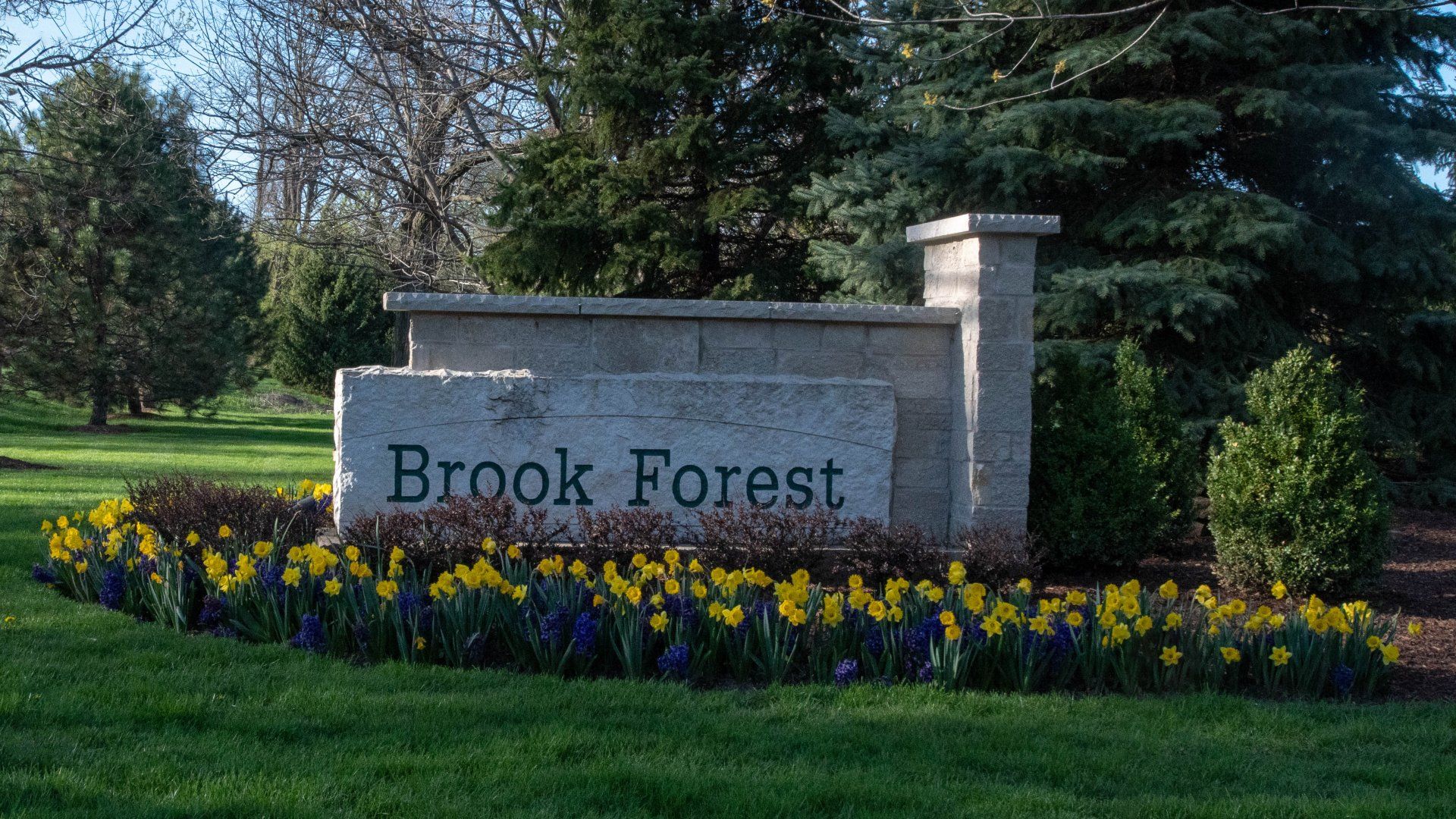 A sign for brook forest is surrounded by flowers and trees