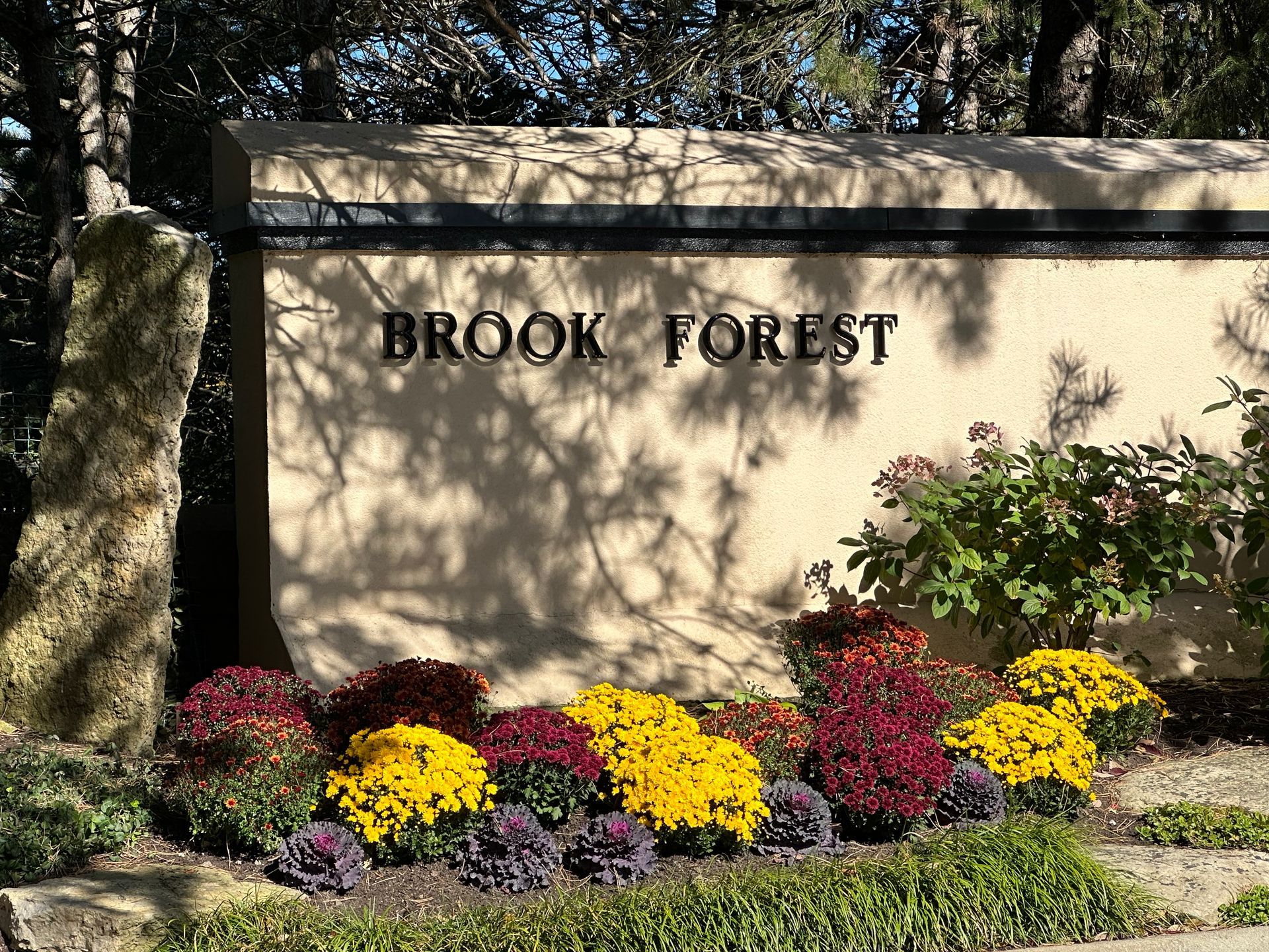 A sign for brook forest is surrounded by flowers and trees.