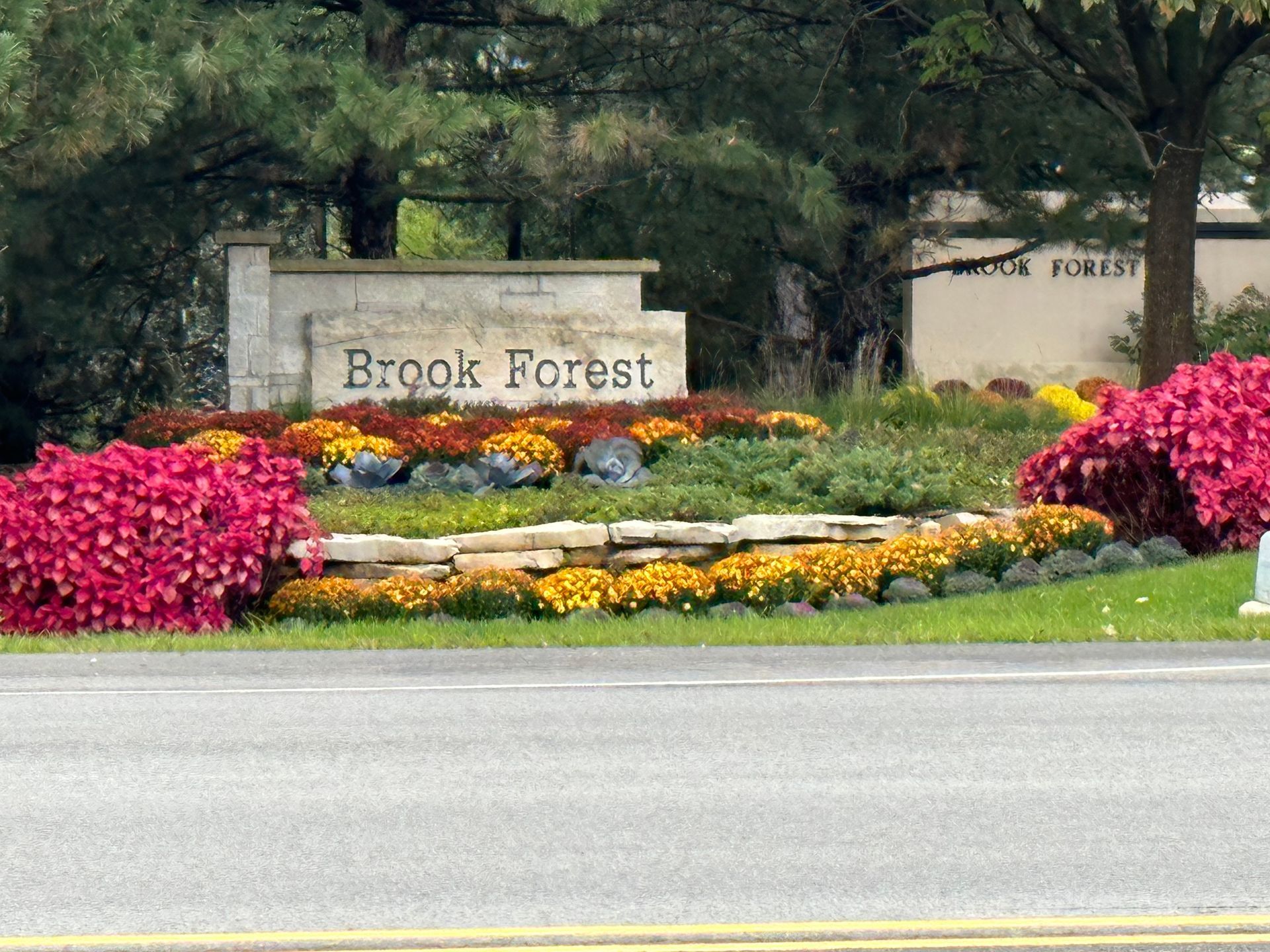A sign for brook forest is surrounded by flowers and trees