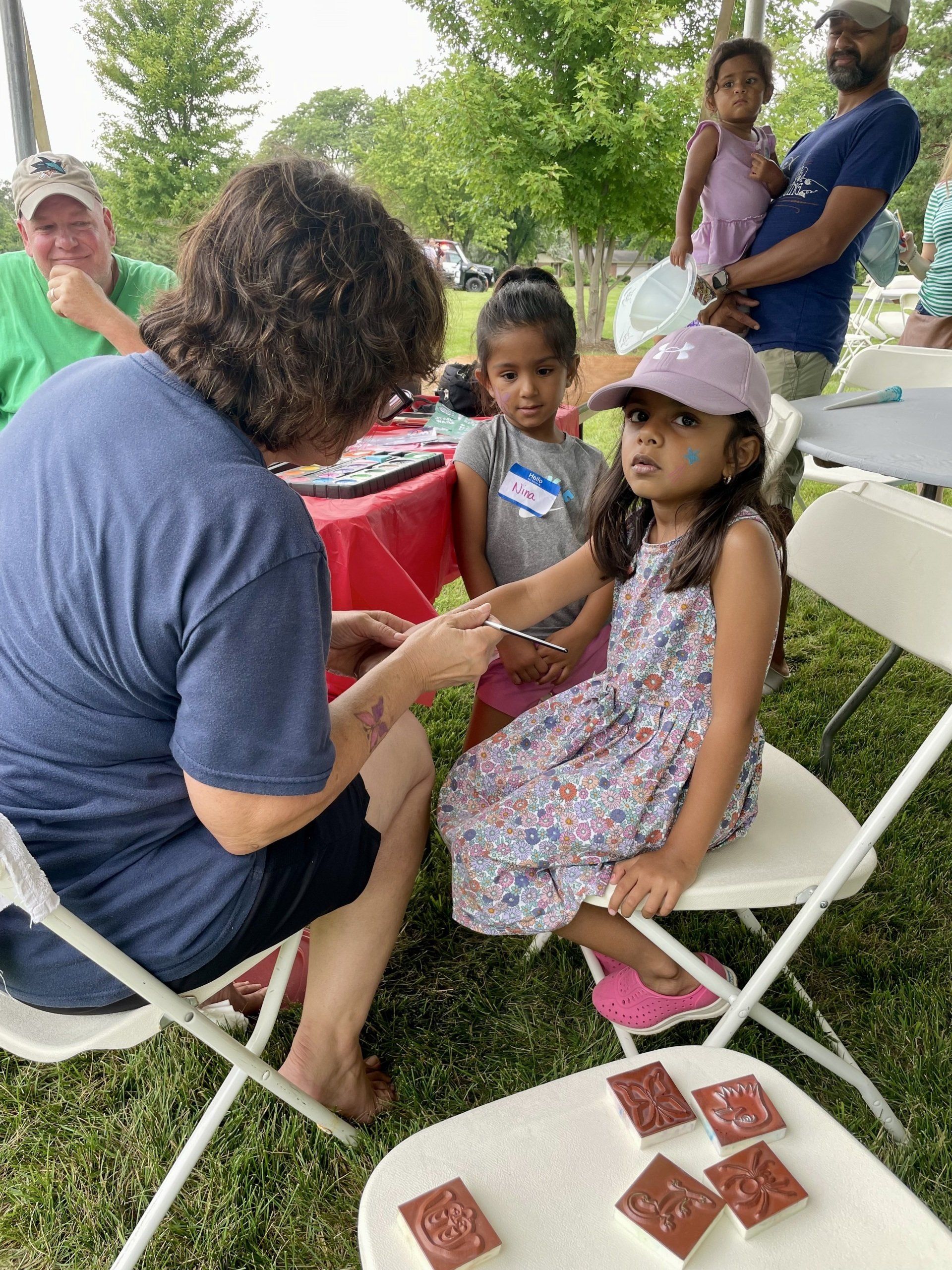 A woman is sitting in a chair painting a little girl 's face.