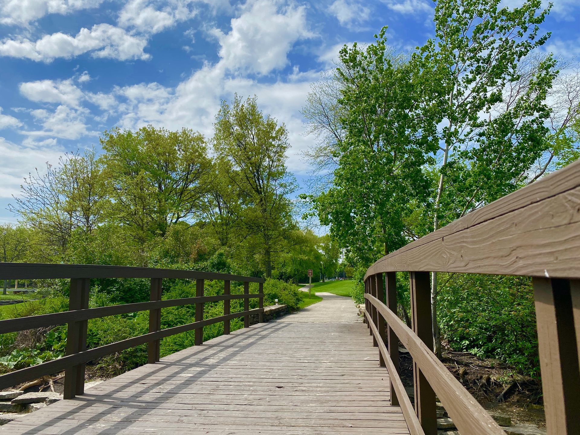 A wooden bridge over a river surrounded by trees on a sunny day.