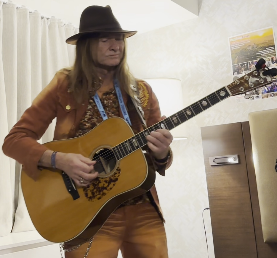 Person in brown outfit and hat playing an acoustic guitar.