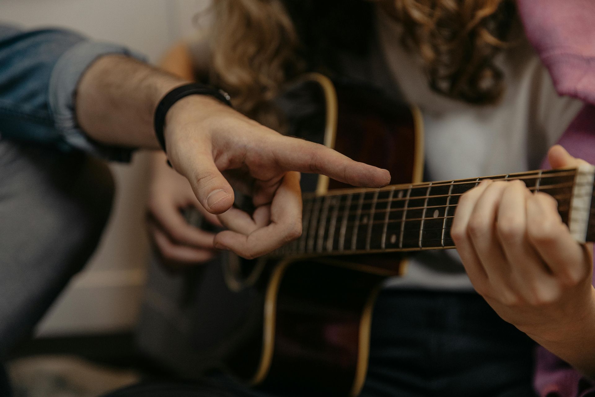 Person's hand showing another how to position fingers on guitar frets for chords.