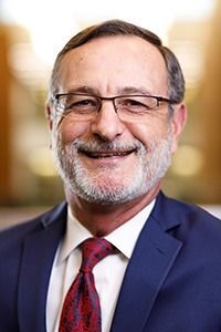 A man with a beard and glasses is wearing a suit and tie and smiling.