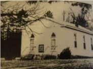 A black and white photo of a church with trees in the background.