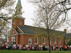 A large group of people are standing in front of a brick church.