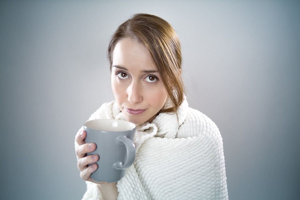 A woman bundled up in a blanket trying to stay warm, sipping coffee