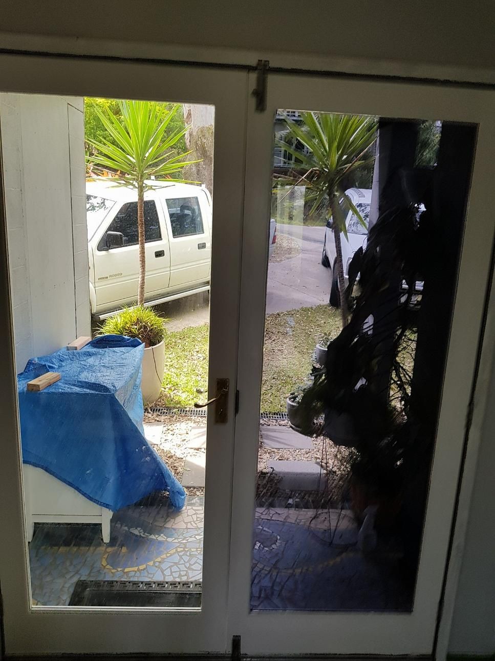 A White Truck Is Parked in The Driveway of A House Behind a Glass Door — Epic Window Tinting in Glenella, QLD