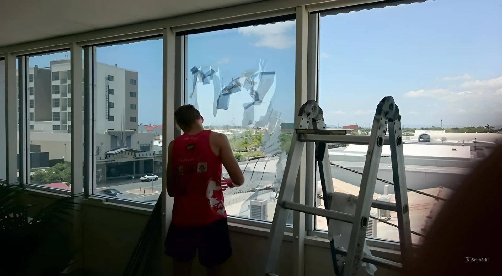 A Man in A Red Tank Top Is Cleaning a Window β Epic Window Tinting in Glenella, QLD