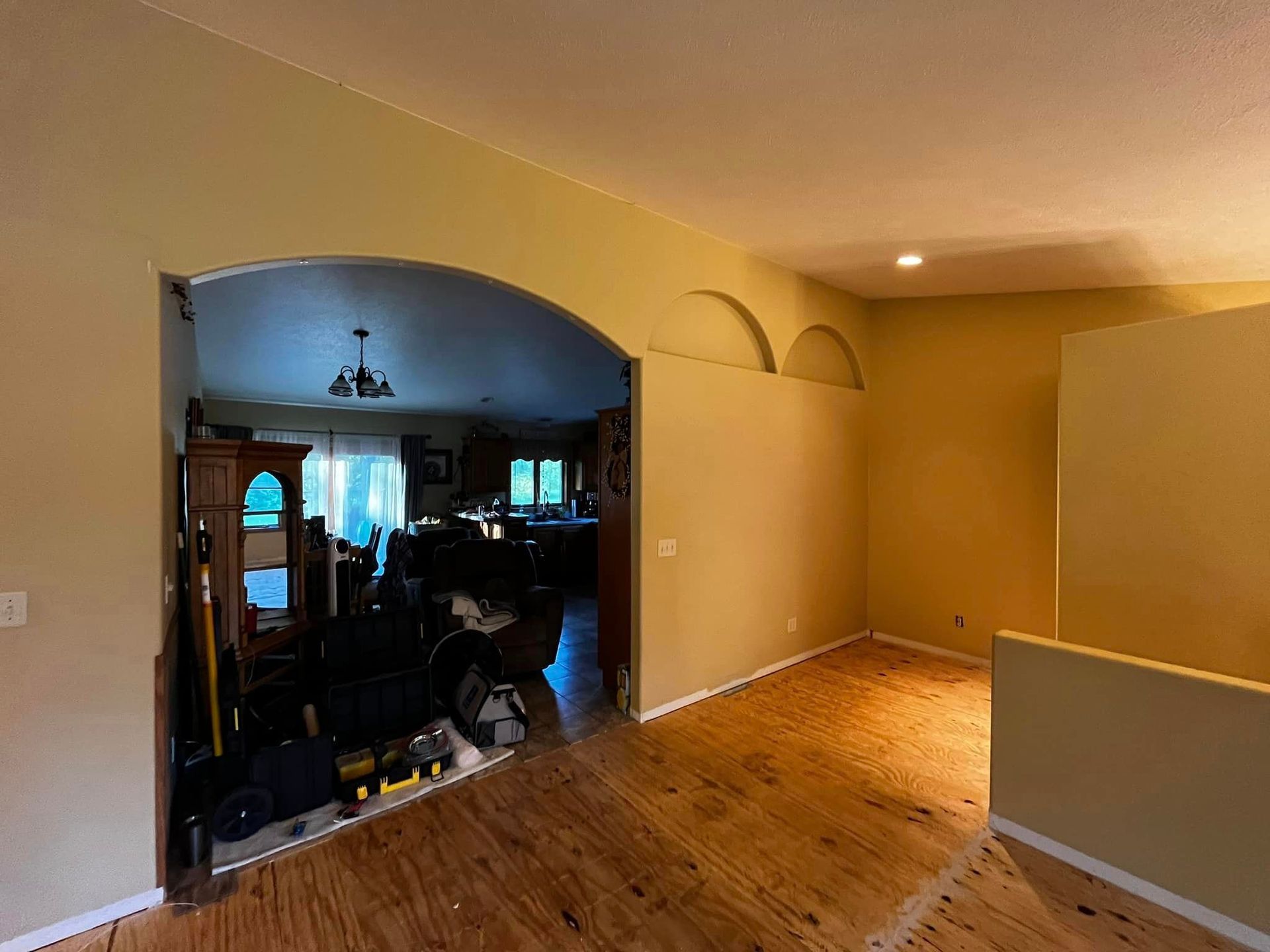 A living room with a wooden floor and a large archway leading to a dining room.
