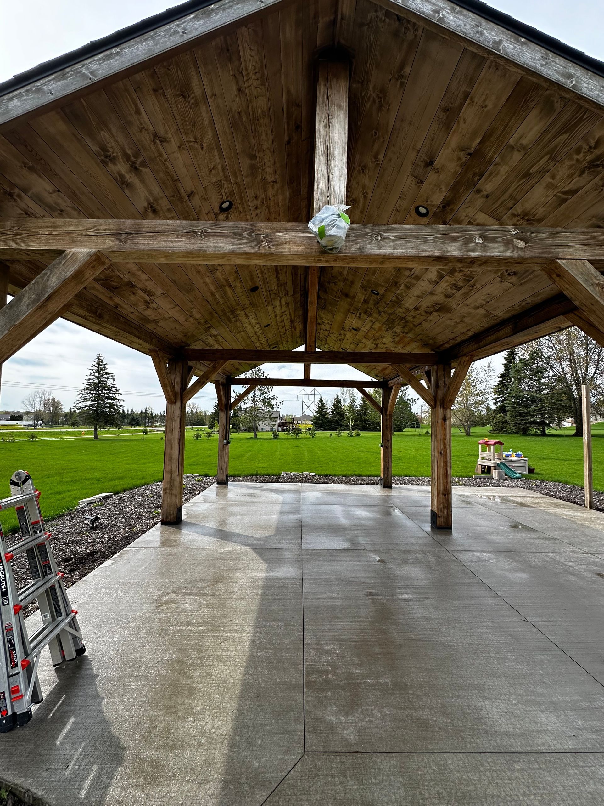 A wooden pavilion with a concrete floor in a park.